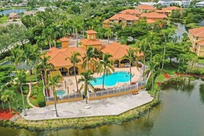 A resort with a swimming pool, palm trees, and a lake.