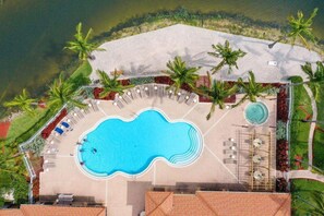 An aerial view of a resort with a central swimming pool, lounge chairs, and palm trees.