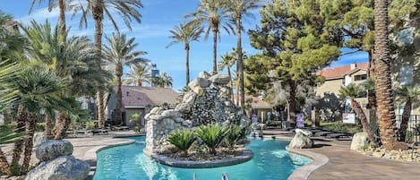 A pool area with a central rock feature, surrounded by palm trees and a stone pathway.
