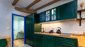 Eine kleine Küche mit grünen Schränken, einer Holz Arbeitsplatte und einem Wasserkocher.