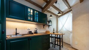 Eine Küche mit dunkelgrünen Schränken, einer Holz Arbeitsplatte, einem Spülbecken und einem Fenster mit transparenten Vorhängen.