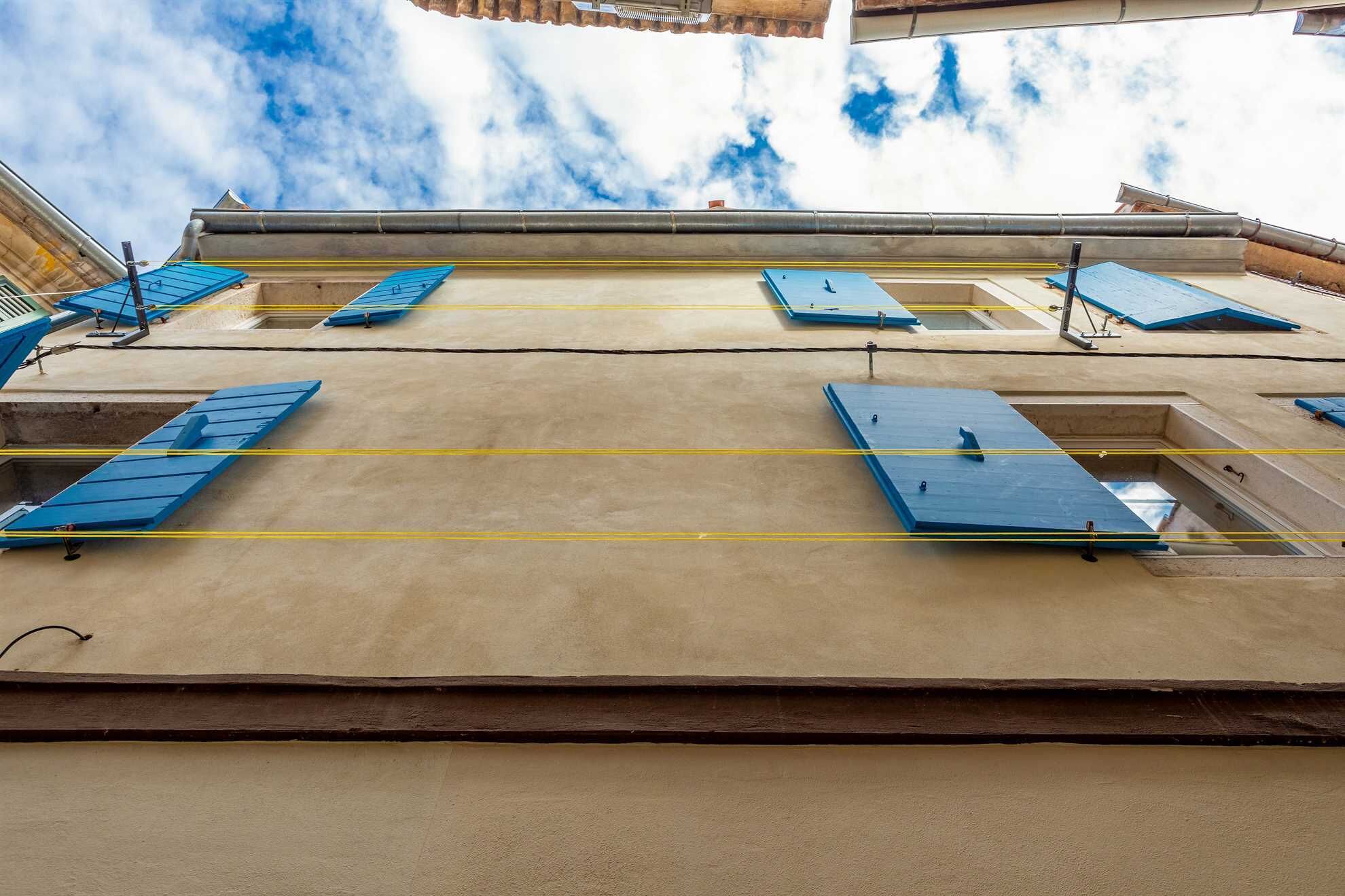 A building with multiple windows, some with blue shutters, and a clear sky with clouds in the background.