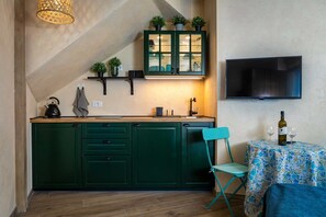 A compact kitchen with green cabinets, a built-in TV, and a small dining area with a floral tablecloth.
