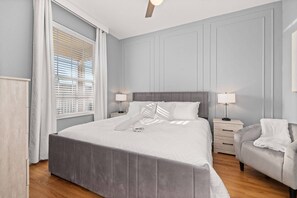 Un dormitorio ordenado con una cama grande, mesitas de noche y una silla.