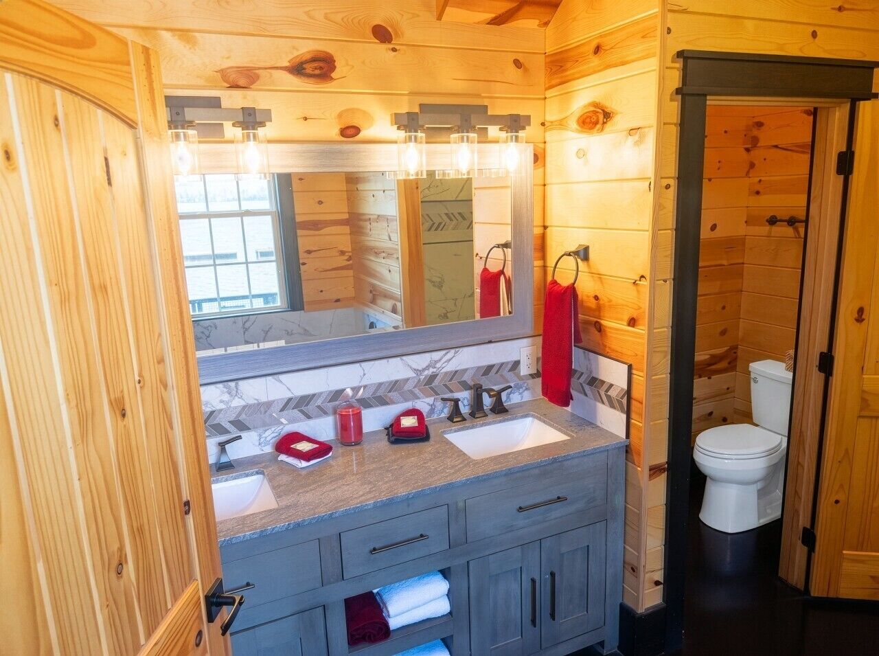 Un baño de cabaña de madera con lavamanos, espejo y retrete.