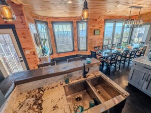 A rustic kitchen with a large island, wooden walls, and a dining area with a view.