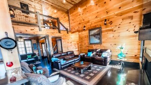 A cozy log cabin interior with a fireplace, leather sofas, and a dining area.