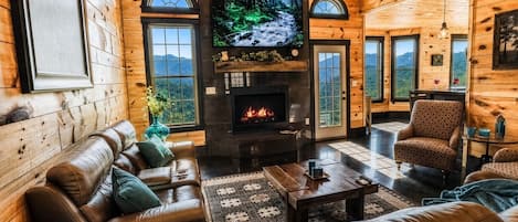 Ein gemütliches Blockhäuschen-Interieur mit Kamin, Ledersitzmöbeln, einem Fernseher und schöner Aussicht.