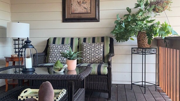 A cozy outdoor seating area with wicker furniture, a framed artwork on the wall, and a hanging plant. - Brookdale Meadows sleeps 6 (Medford)