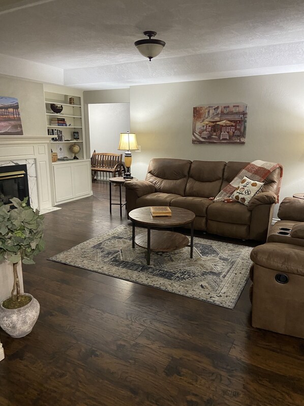 A living room with a brown sofa, a coffee table, and a fireplace. There is a rug on the floor and a painting on the wall.