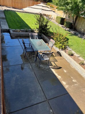 A patio with a table and chairs, a small garden area, and a wooden fence in the background.