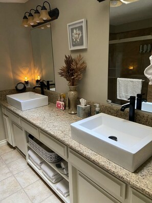 A bathroom with two sinks, a mirror, a vase with dried flowers, and a towel rack.
