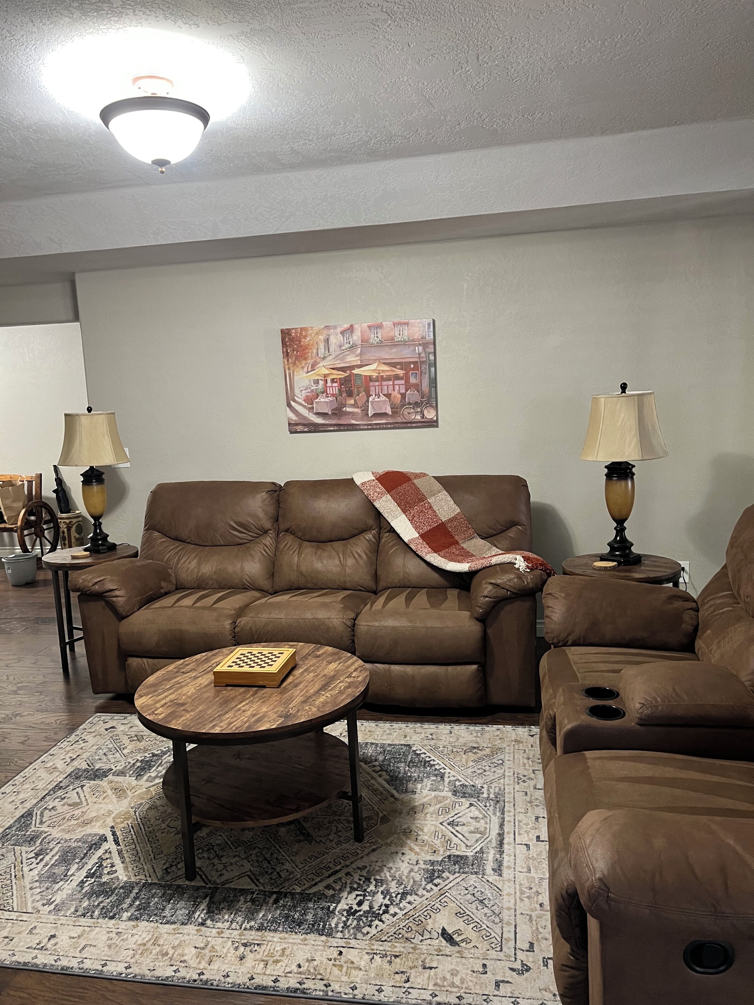 A living room with a brown leather sofa, a wooden coffee table, two lamps, a painting on the wall, and a patterned rug.