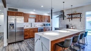 A modern kitchen with a large island, stainless steel appliances, wooden cabinets, and a bar area with stools. - South Scottsdale Poolside Getaway! (Scottsdale)