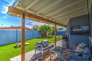 Relax in a shaded patio area with a sofa and table, surrounded by a neatly trimmed lawn and a blue wall.