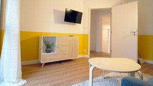 Una sala de estar moderna con un televisor de pantalla plana montado en la pared, un mueble de madera con una planta y una mesa redonda con una silla.