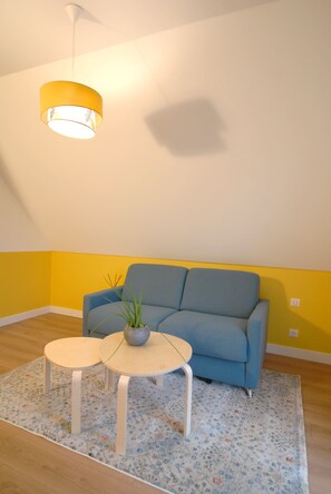 A room with a blue sofa, two small round tables, a potted plant, and a yellow pendant light.