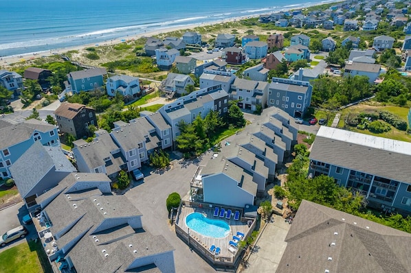 A residential area with a swimming pool, houses, and a beach in the background.