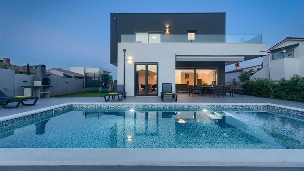 Een modern huis met twee verdiepingen en een zwembad op de voorgrond.