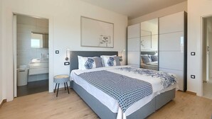 Een moderne slaapkamer met een groot bed, een nachtkastje, een stoel, een kledingkast en een spiegel.