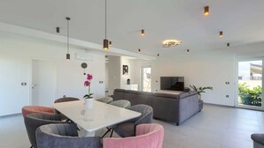 Een moderne woonkamer met een eethoek, een grijze bank en een televisie.