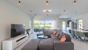 Een moderne woonkamer met een modulaire bank, een flatscreen televisie en een eethoek met een tafel en stoelen.