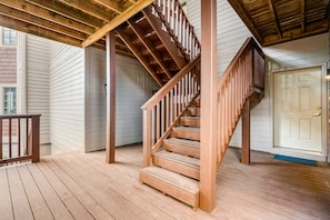 A wooden staircase leading to a second floor in a house with white siding and a wooden deck.