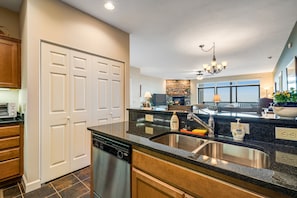 A modern kitchen with a dishwasher, double doors, granite countertops, and a large window.