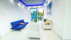 Un salon moderne avec un canapé bleu, un fauteuil blanc et une petite table blanche.