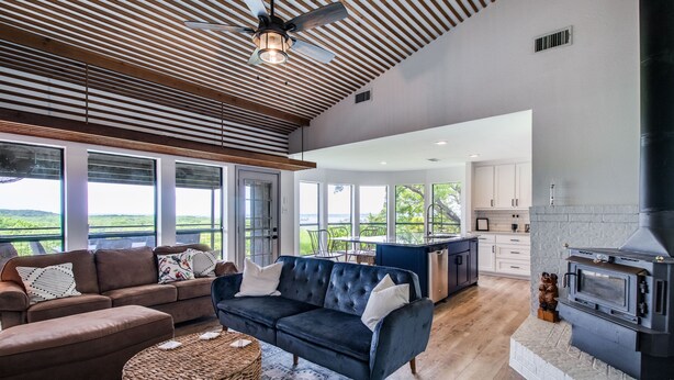 A spacious living area with a dark blue sofa, a brown sofa, and a wicker ottoman. There is a fireplace and a kitchen area visible in the background. - Lake views from The Byrd House (Pottsboro)