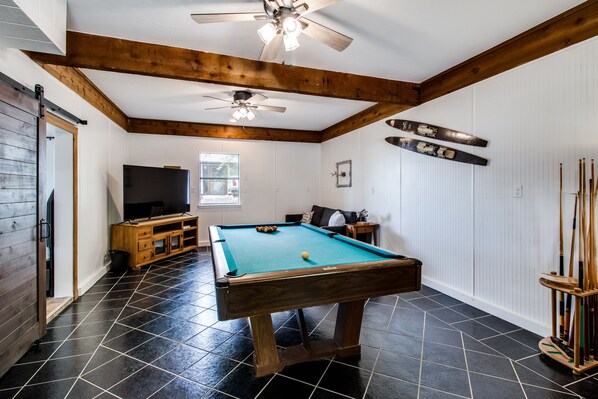 A pool table in a room with wooden beams, a ceiling fan, and a television. - Lake views from The Byrd House (Pottsboro)