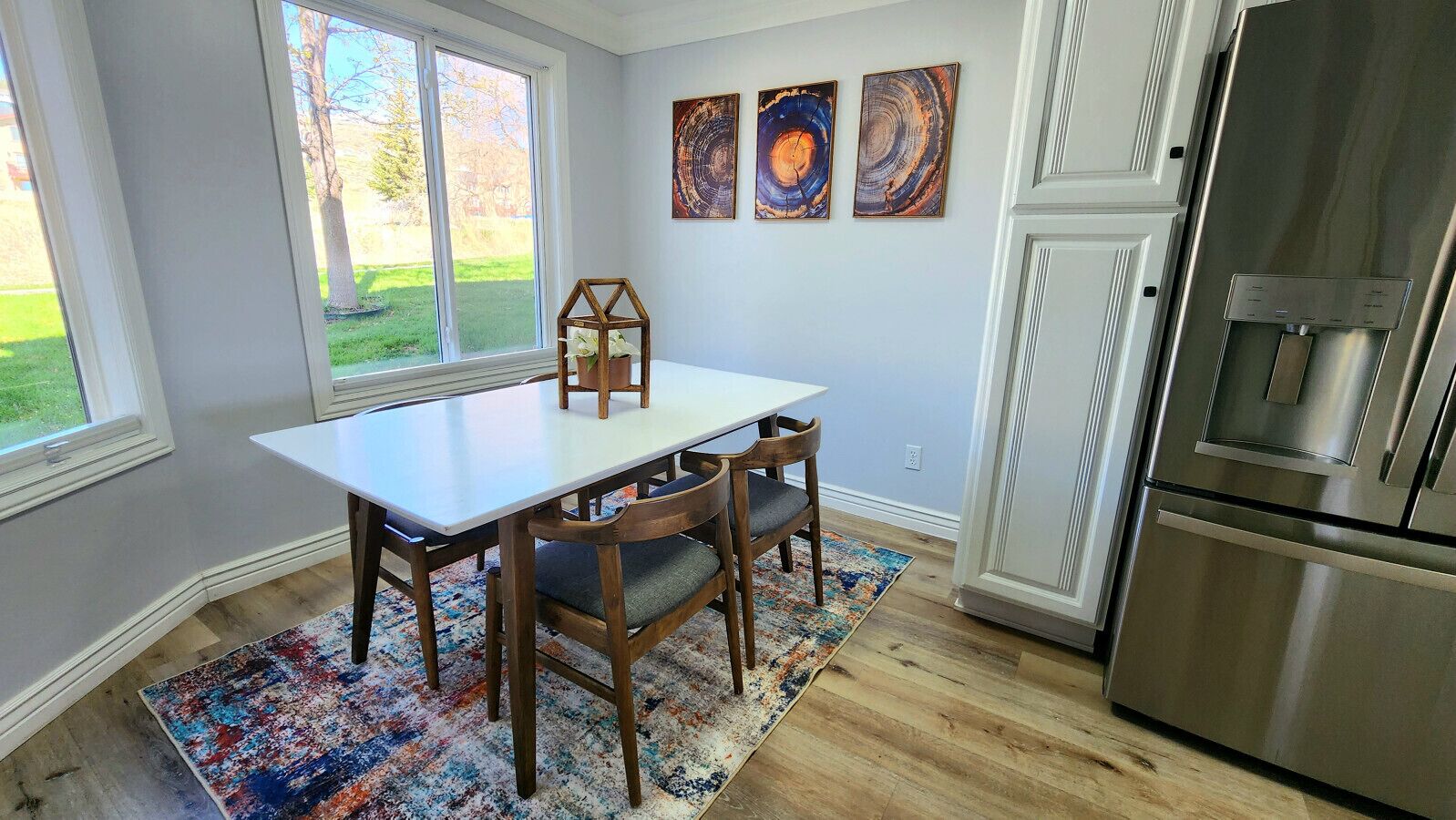 A kitchen with a white table, wooden chairs, a rug, and a stainless steel refrigerator.