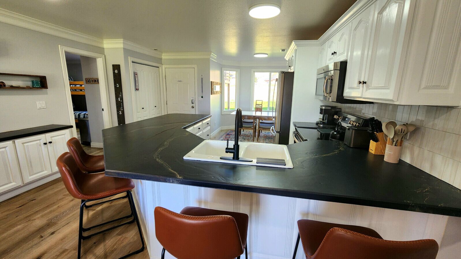 Een keuken met een zwart aanrecht, witte kasten en een centraal eiland met krukken.