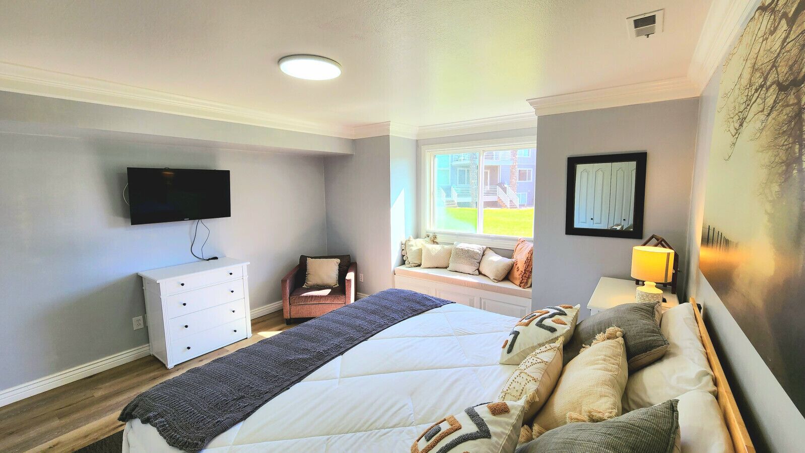 Une chambre à coucher comprenant un lit, une télévision, un coin fenêtre aménagé en siège, une commode et une lampe.