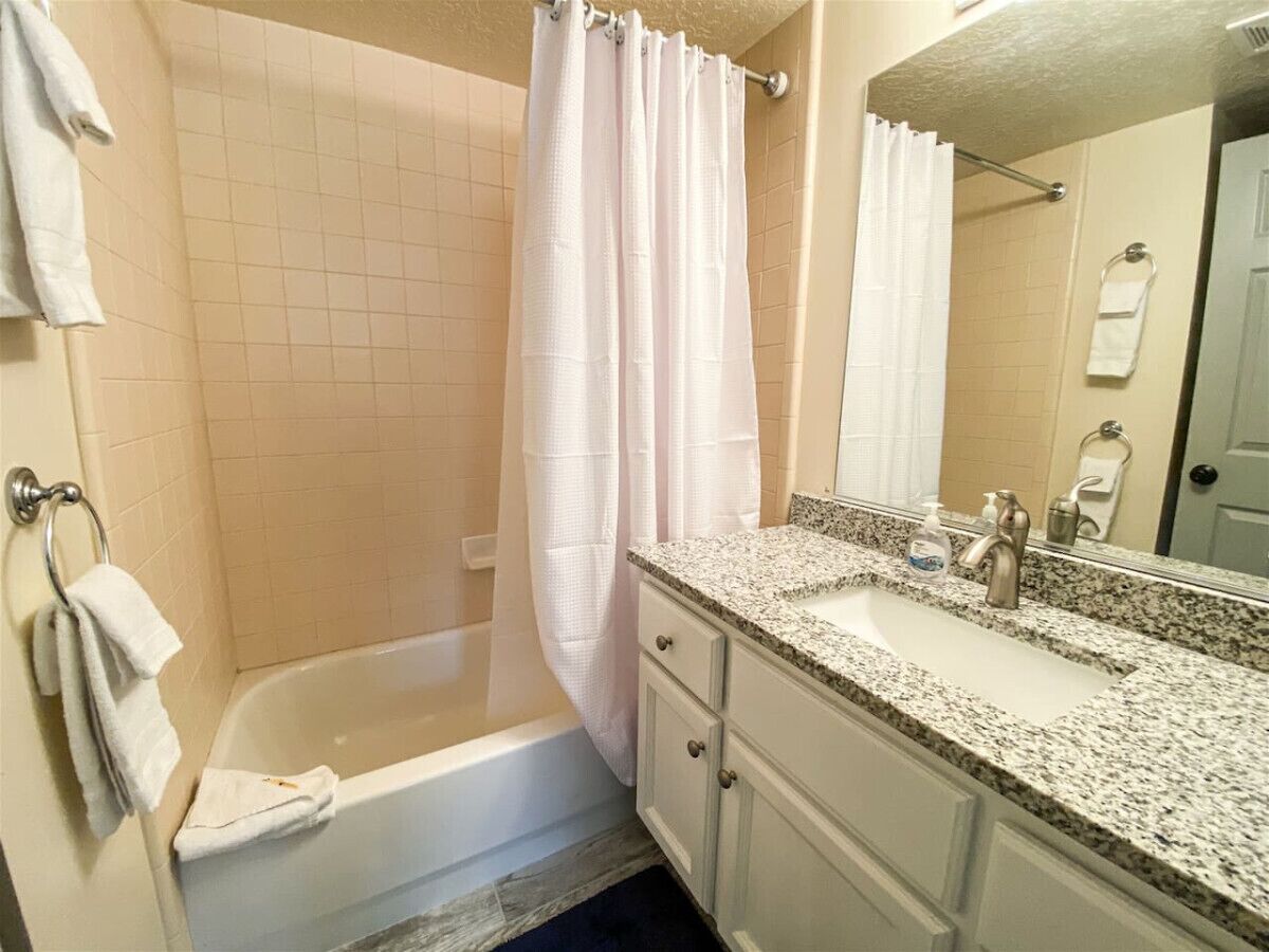 A bathroom with a bathtub, a shower curtain, a sink with a mirror, and a towel rack.