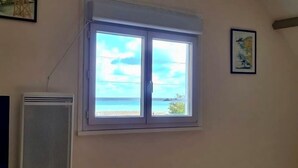 A room with a large window offering a view of the sea. There is a wall-mounted air conditioner to the left. - Near Paimpol, duplex Beach Bréhec 200m (Plouézec)