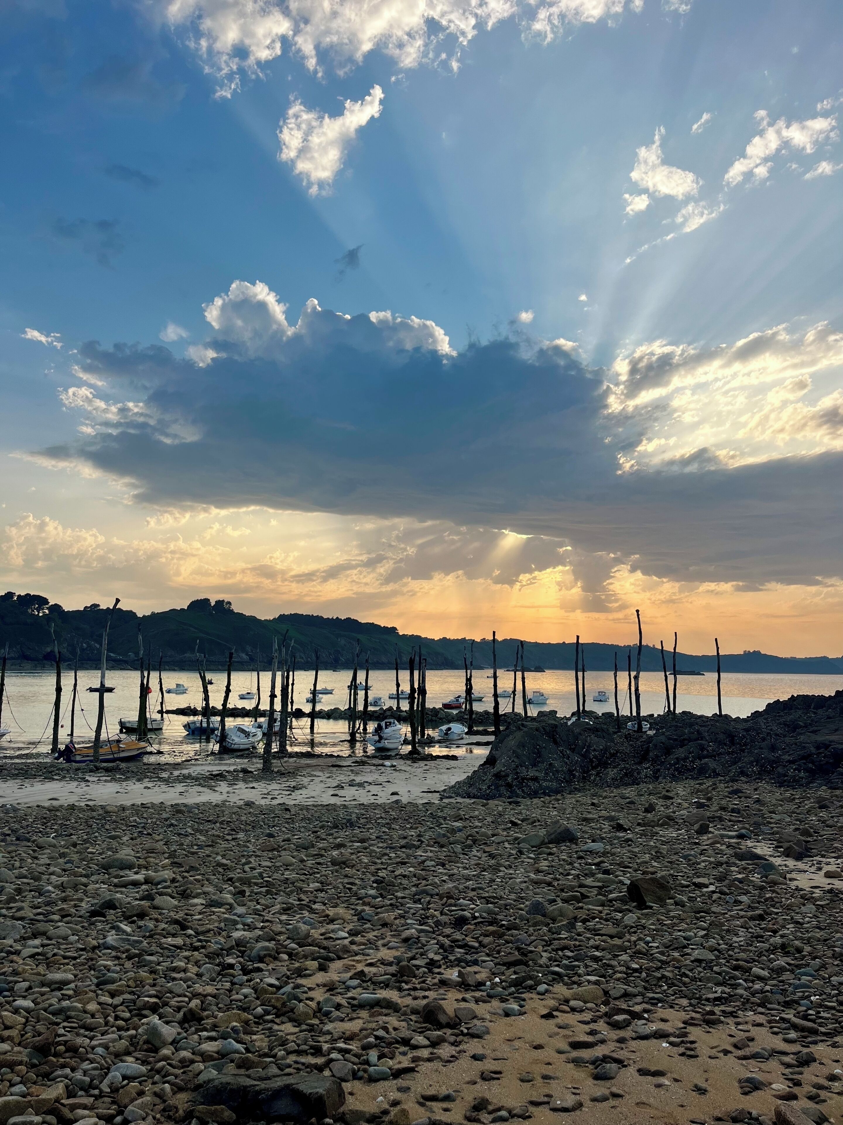 Une plage rocheuse avec des bateaux et une mer calme sous un ciel nuageux.