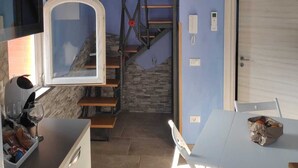A compact kitchen with a stone wall, a wooden staircase, and a white dining table. - Mami Luroviga (Vico Equense)