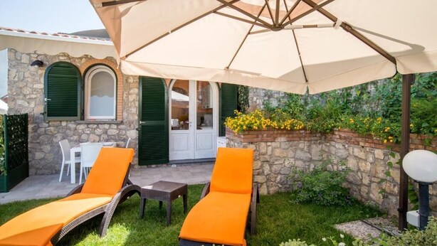 A stone building with a covered patio, two orange lounge chairs, and a table under a large umbrella. - Mami Luroviga (Vico Equense)