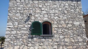 A stone building with a tiled roof and a small window with green shutters. - Mami Luroviga (Vico Equense)