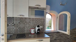 A compact kitchen with white cabinets, a patterned backsplash, a built-in microwave, and a window with an archway. - Mami Luroviga (Vico Equense)