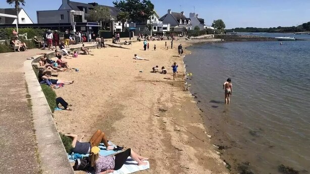 Ein Strand mit badenden Menschen und Spaziergängern am Ufer.