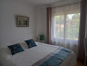 Ein ordentlich gemachtes Bett mit einer gesteppten Kopfteil, ein gerahmtes Bild an der Wand und ein Fenster mit Vorhängen.