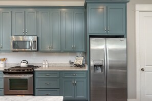 A kitchen with teal cabinets, stainless steel appliances, and a marble countertop.