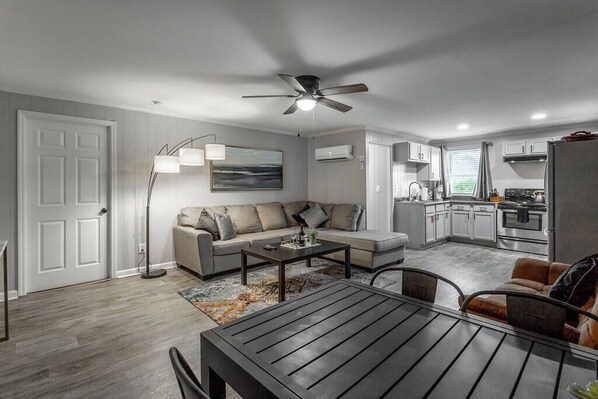 A modern living room with a sofa, coffee table, and a dining table. There is a kitchen area with cabinets and appliances. - Suite 203 - Felicity at Rock Spring Resort (Rock Spring)