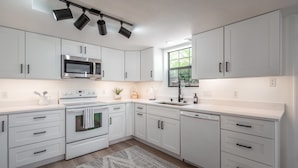 Una cucina moderna con mobili bianchi, un forno a microonde in acciaio inossidabile, un forno integrato e una lavastoviglie.