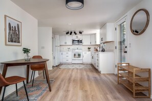 A modern kitchen with white cabinets, a microwave, and a stove. There is a dining area with a table and chairs, and a rug on the floor.