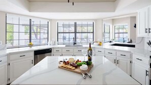 A modern kitchen with white cabinetry, a central island with a cheese board, and large windows. - Paradise Palace-Heated Pool/Spa-Guest House & More (Scottsdale)