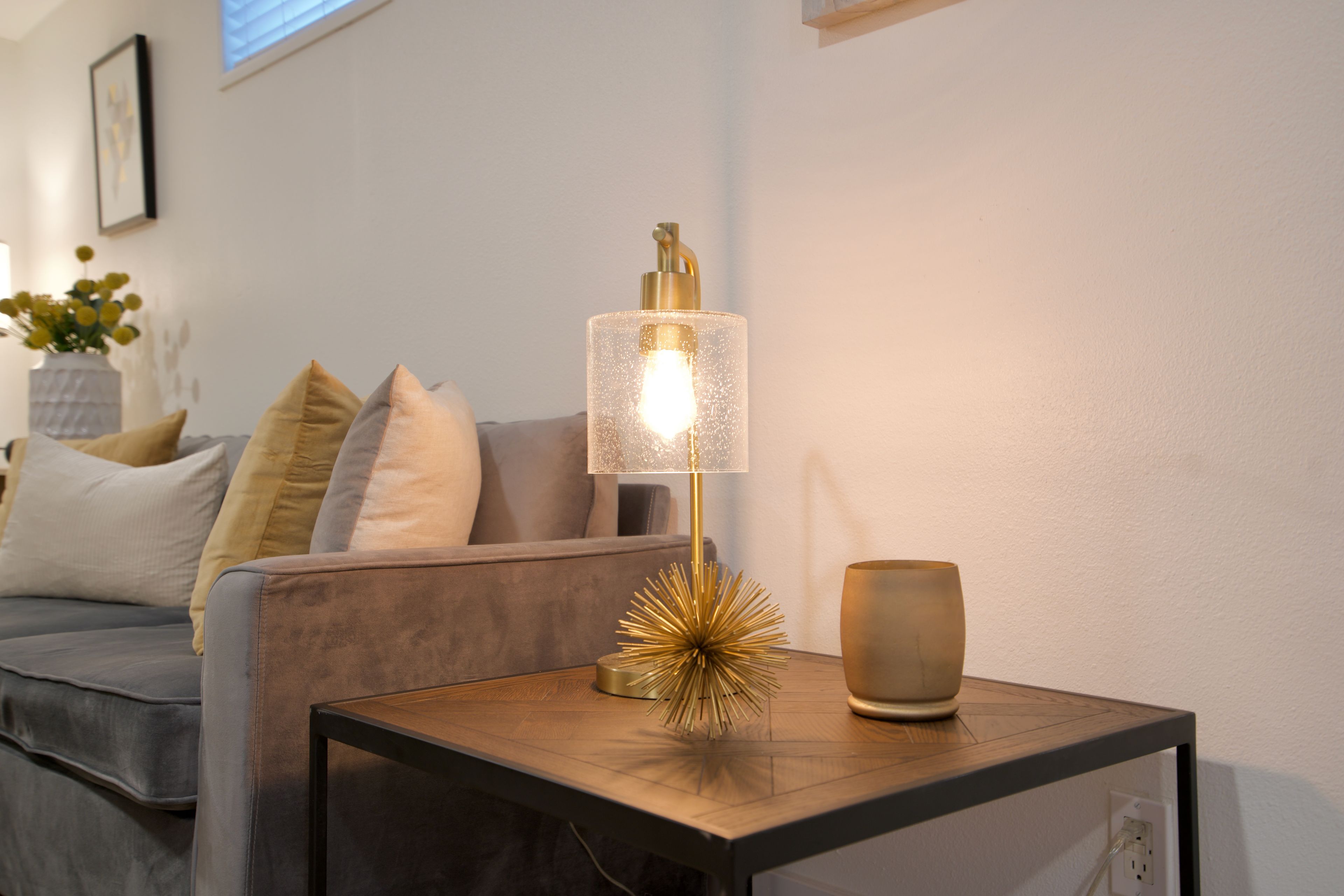 A modern living room with a sofa, a small table with a lamp, and decorative items.