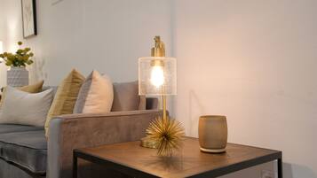 A modern living room with a sofa, a small table with a lamp, and decorative items.